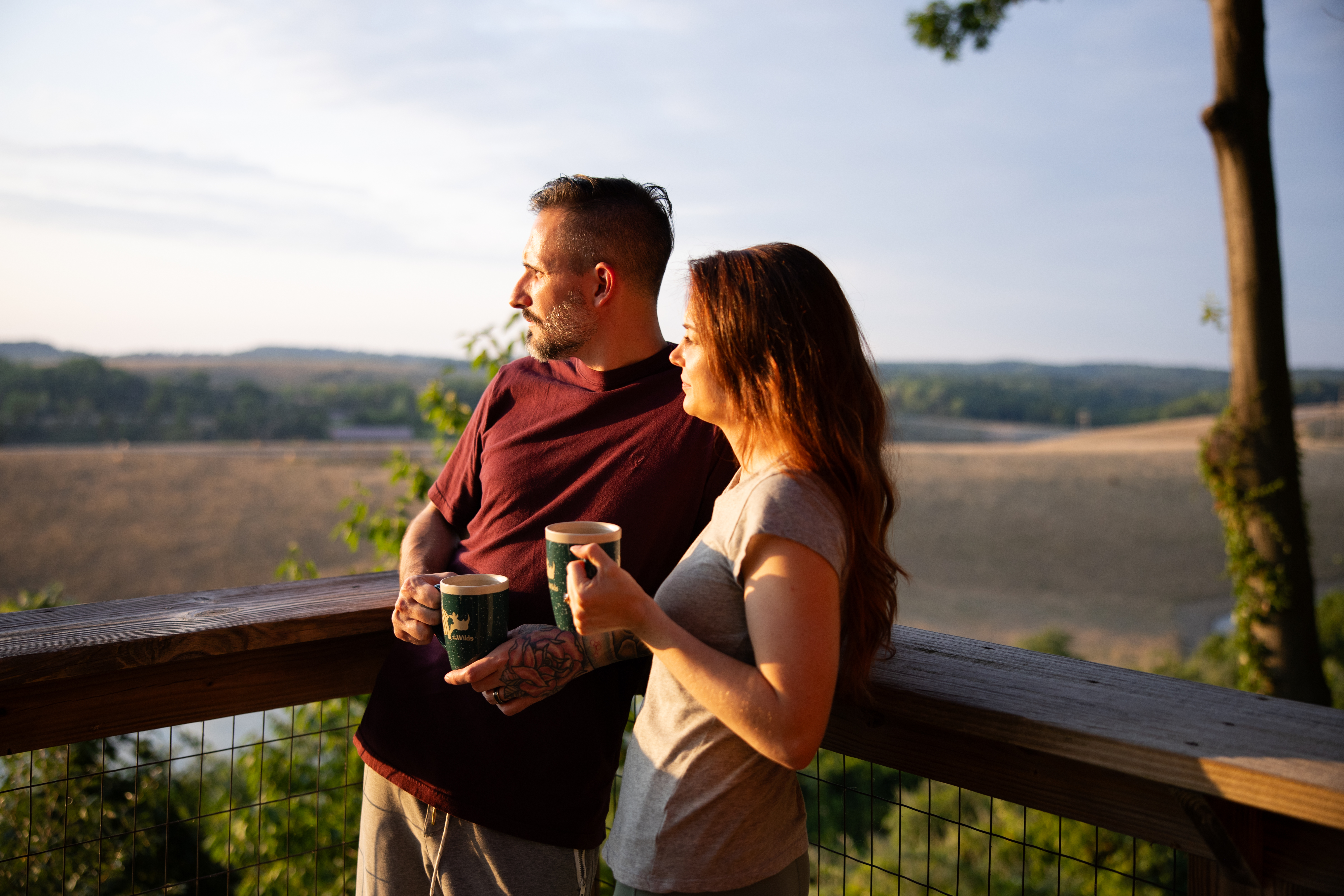 two people looking over a pasture and leaning on wooden fence
